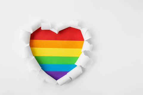 White paper background with paper peeled to reveal rainbow heart