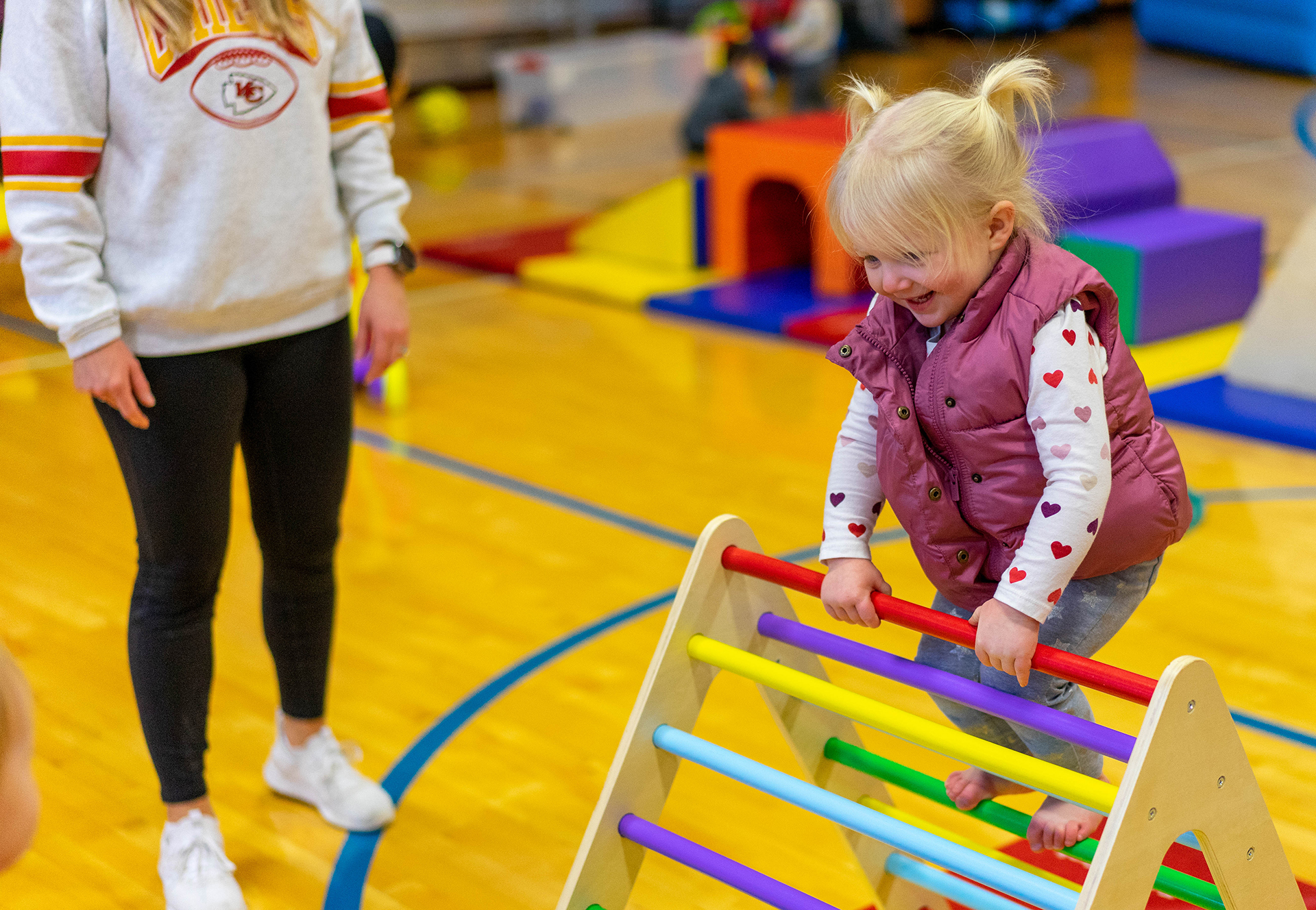 A small girl climbs on a colorful play ladder