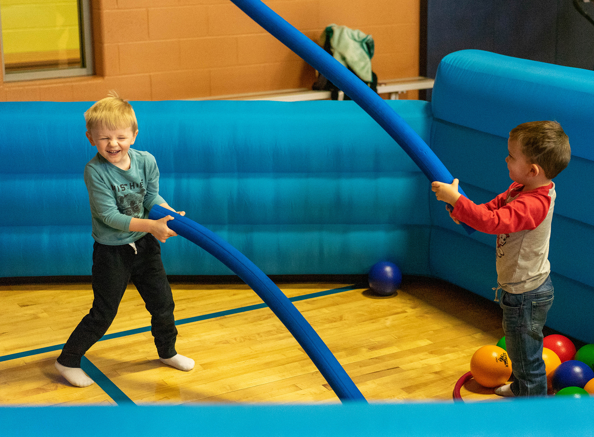 Two children playfully swinging pool noodles at each other