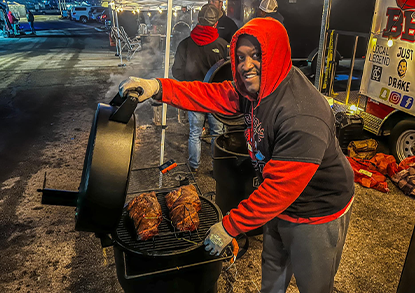 A man wearing a red hoodie and black t-shirt shows off his smoked meats at the Qlathe BBQ Championship