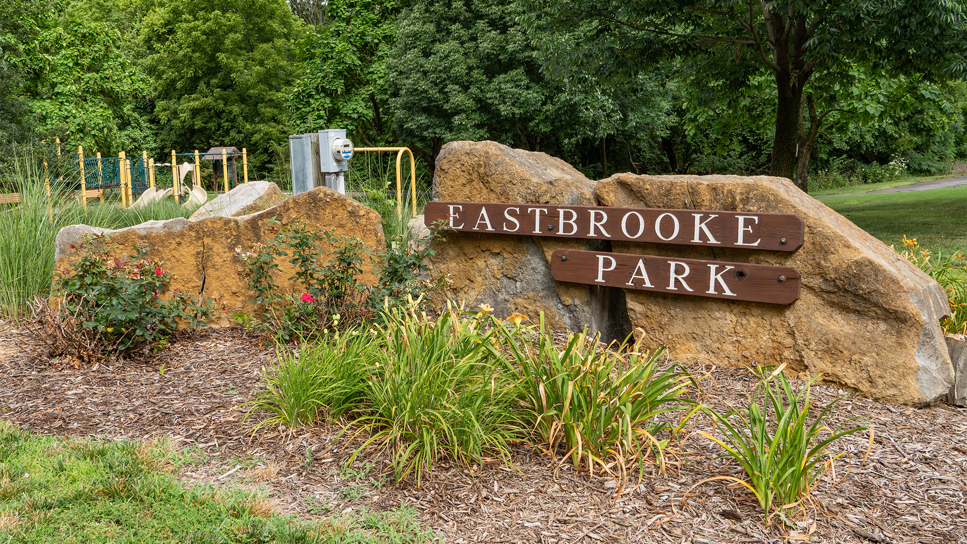 A wooden sign that reads "Eastbrooke Park" with a playground in the background