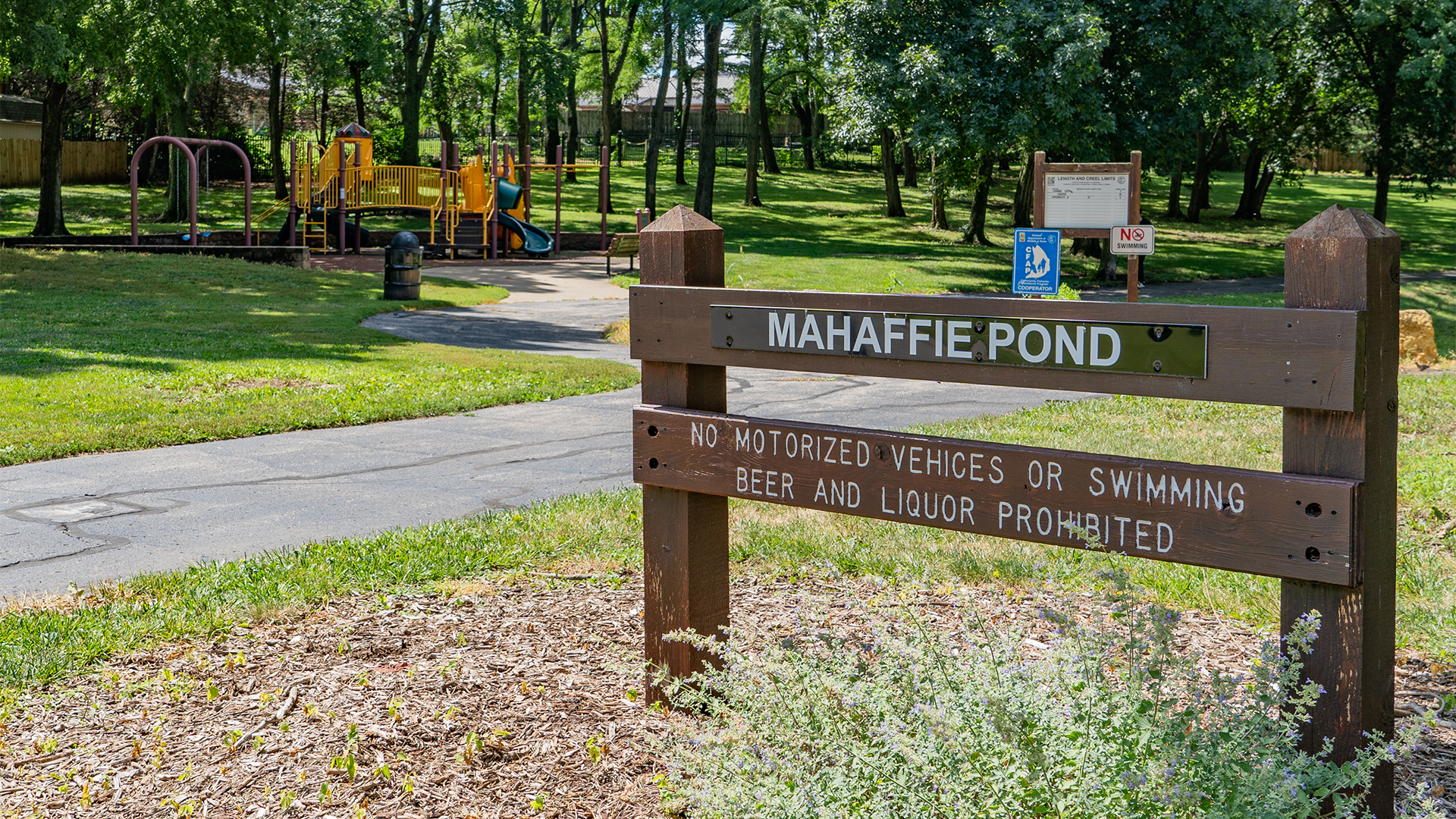 Mahaffie Pond wooden sign with park rules and playground in the background