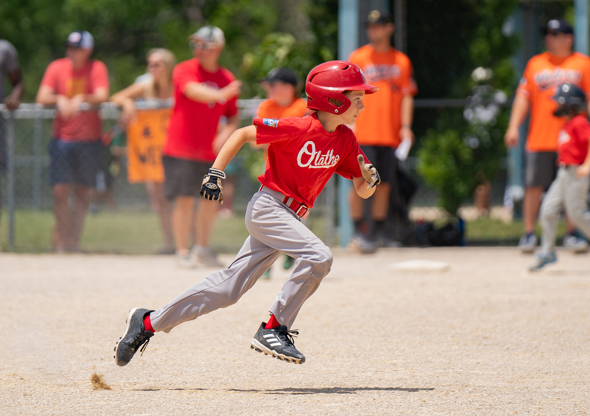 A baseball player wearing a red shirt and helmet rounds the bases