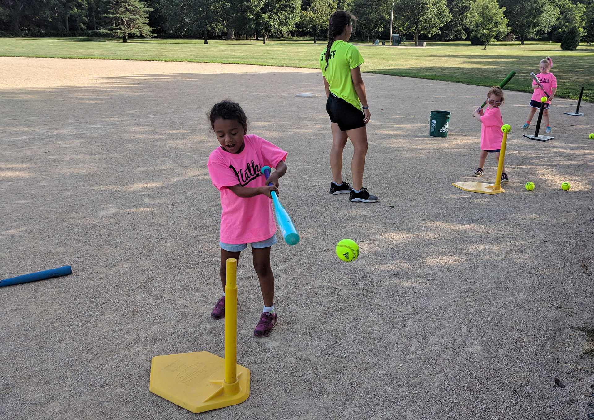 A girl wearing a pink shirt swings a bat at a softball on a tee