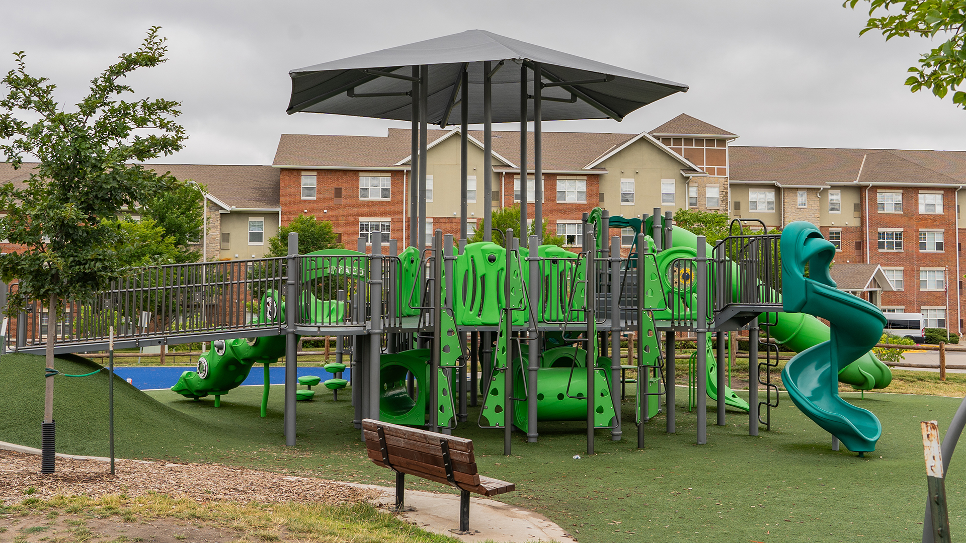 Gray and green playground structure with a wooden bench