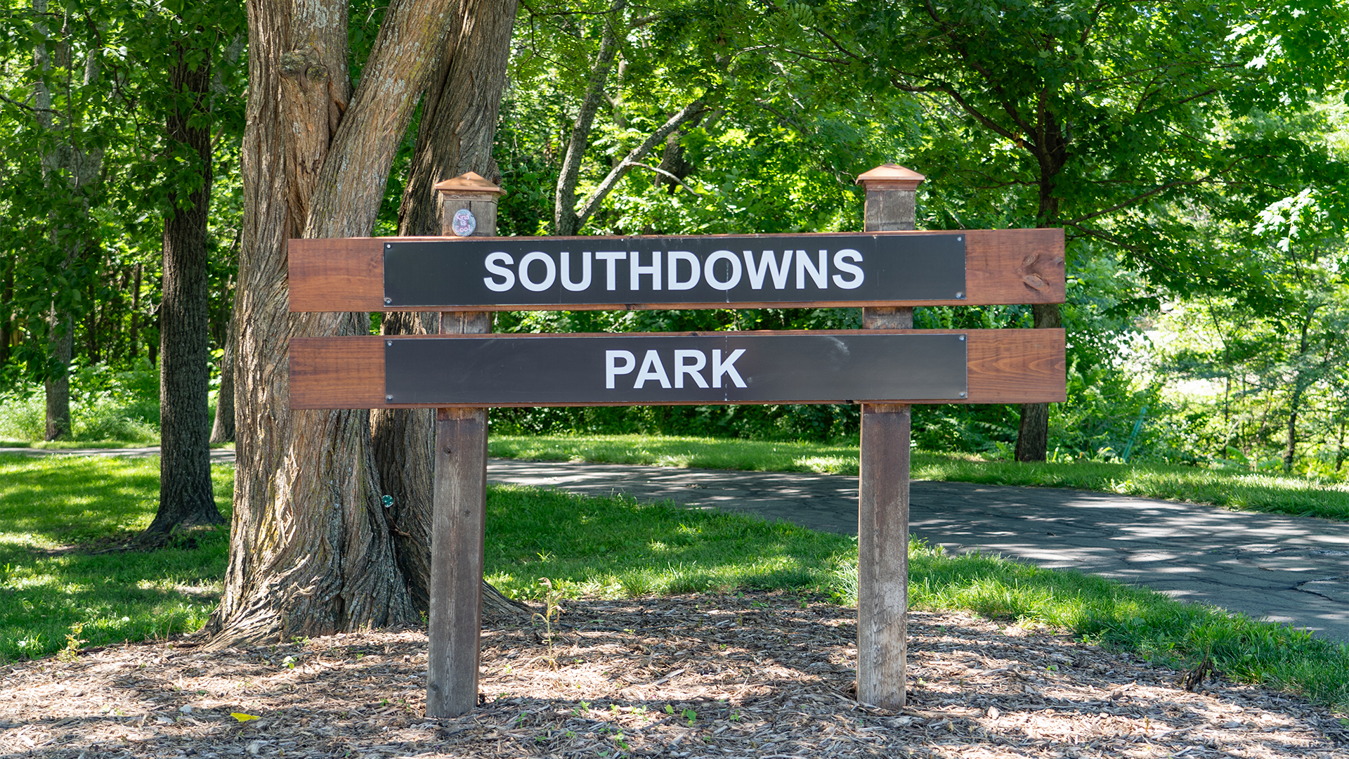 Wooden sign that states "Southdowns Park" with concrete walking trail behind it