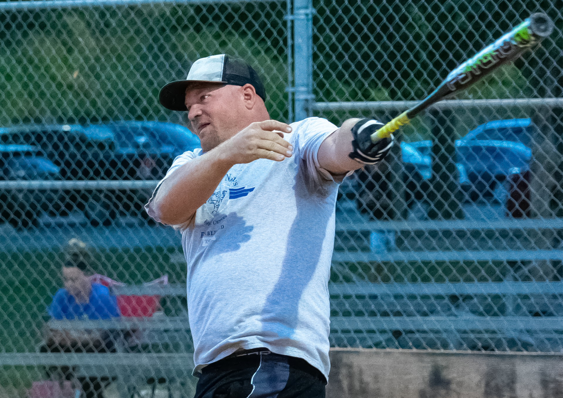 An adult male swings a softball bat