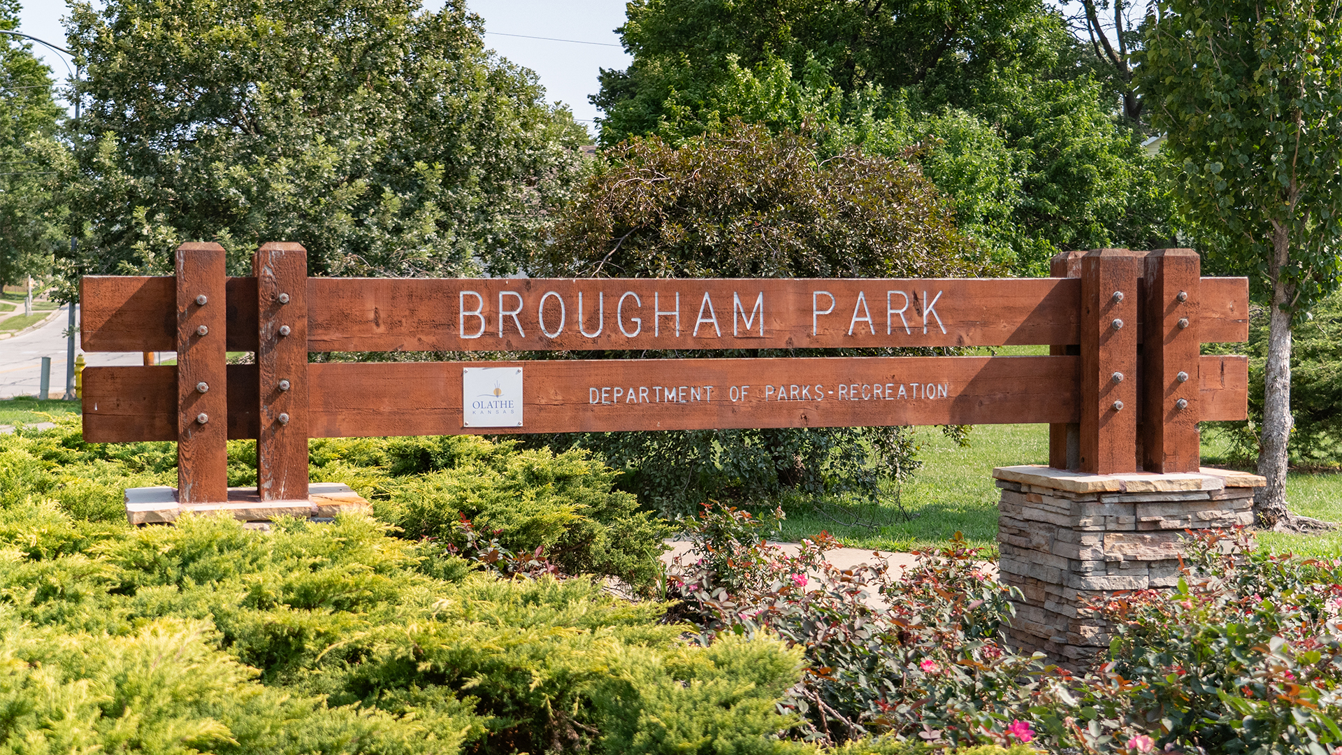 Wooden sign surrounded by bushes that states "Brougham Park" and "Department of Parks-Recreation"