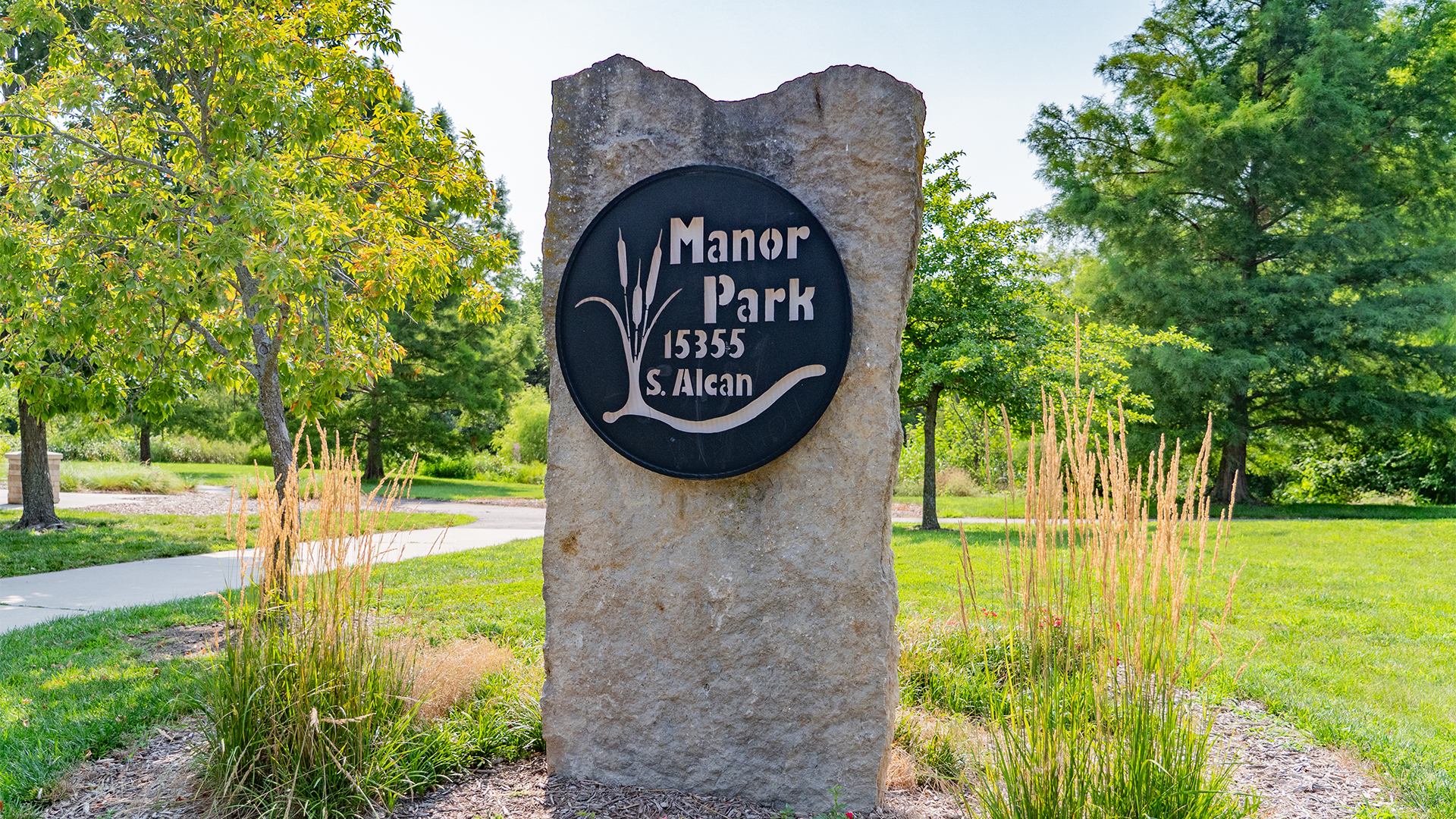 Stone with circular metal plate that reads "Manor Park 15355 S. Alcan"