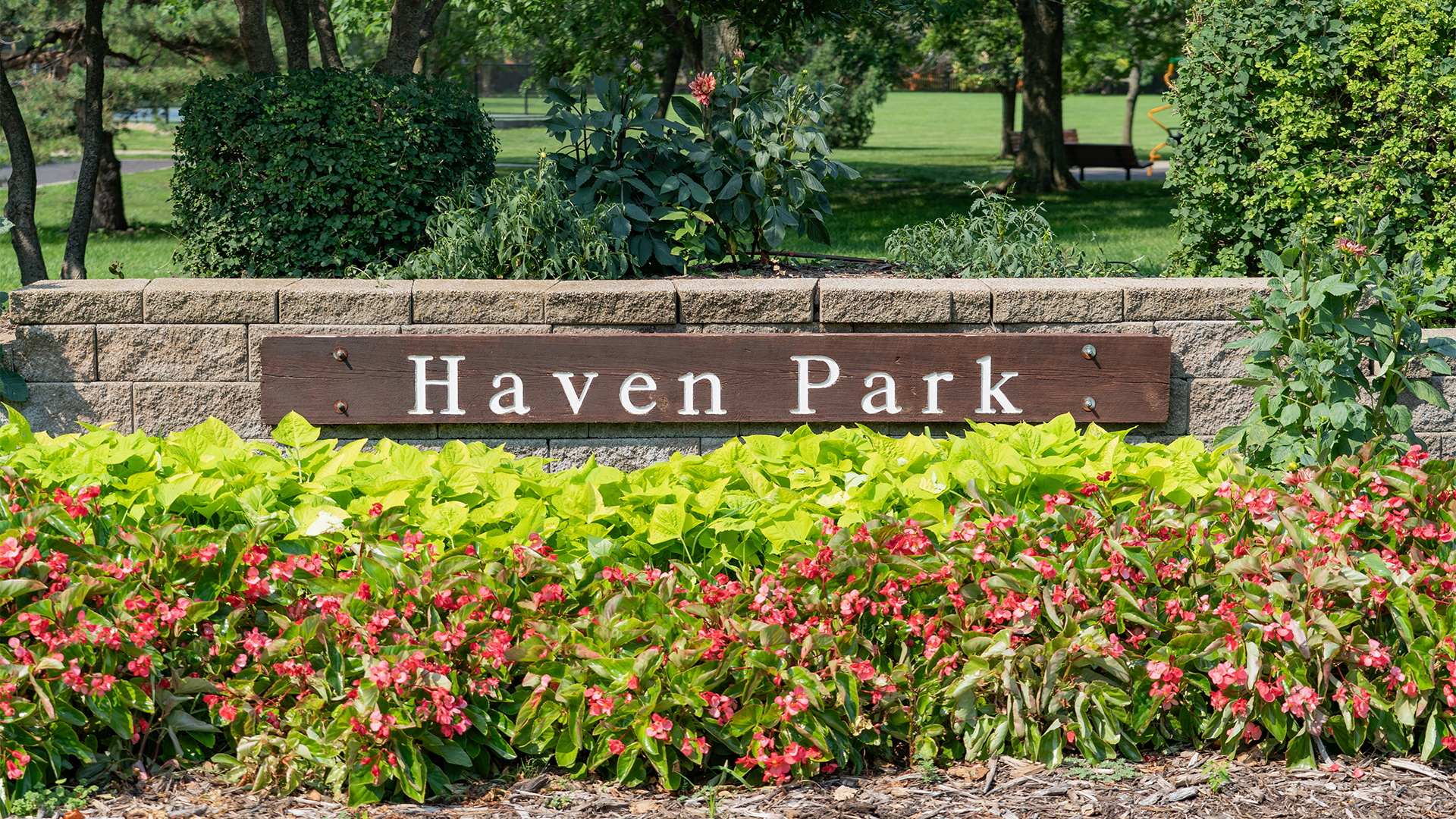 Wooden sign that states "Haven Park" on a stone brick wall with plants in front