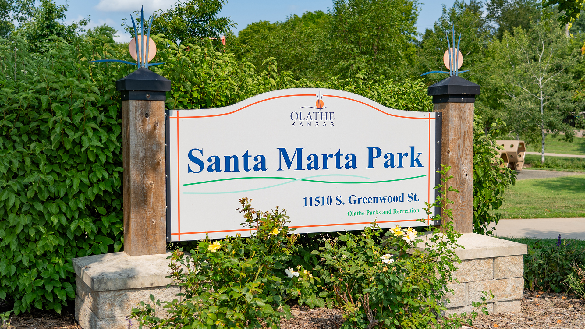 Sign that states "Santa Marta Park" and "11510 S. Greenwood St. Olathe Parks and Recreation" with stone brick base and wooden beams at either side