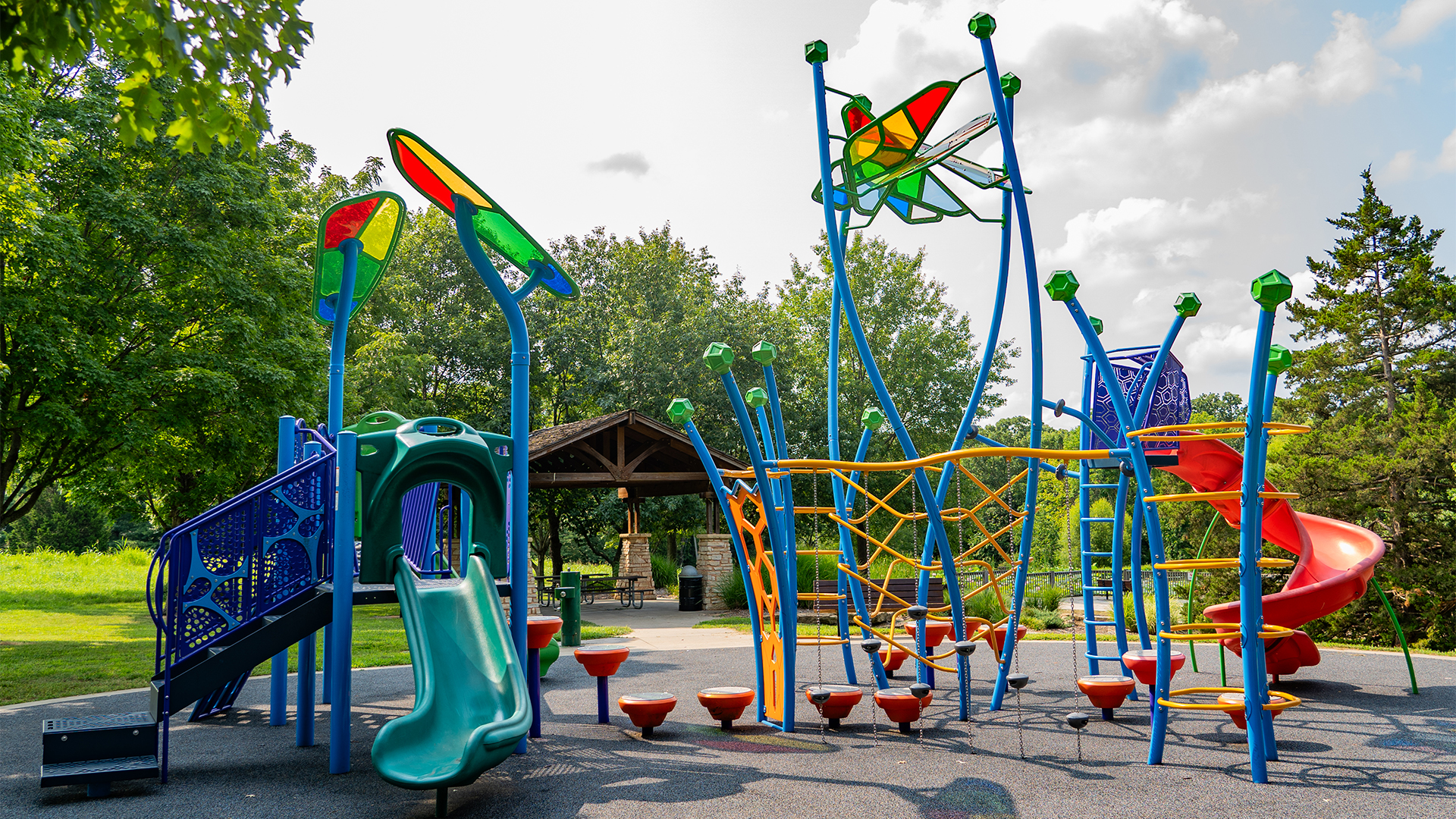 Multicolored playground structure with slides and park shelter in the background