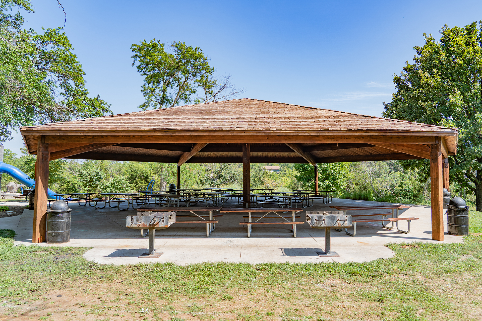 Park shelter with picnic tables, two charcoal grills, and trash cans