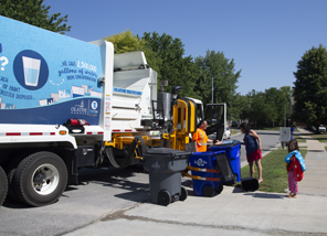 Recycling Truck picking up a blue recycling cart as homeowner looks on.